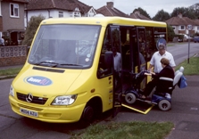 The bus driver watches whilst a passenger boards the bus in a mobility scooter